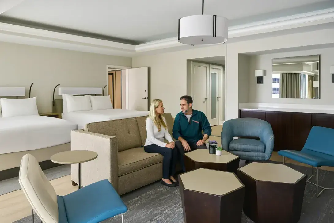 A middle-aged couple relaxing together in Hyatt Regency hotel suite with two beds and lounge area